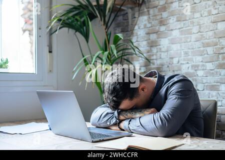 Erschöpfter junger kaukasischer Angestellter Schlafplatz im Büro Überarbeit bei der Erstellung des Berichts. Müde Männer schlafen ein, schlendern am Arbeitsplatz ab, arbeiten spät, um die Frist einzuhalten. Ermüdung, Erschöpfungskonzept. Stockfoto