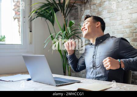 Glücklicher Geschäftsmann, der Kopfhörer trägt und am Arbeitsplatz einen Song singt, lustiger Mitarbeiter oder Freiberufler mit dem Laptop, genießt Lieblingstitel, hört Musik, tanzt, macht Spaß in der Pause Stockfoto