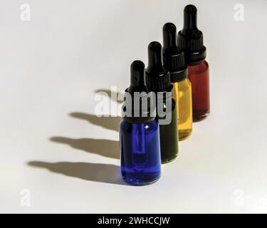 Vier Tropfflaschen aus Glas, gefüllt mit blauer, grüner, gelber und roter Flüssigkeit, die dunkle Schatten auf weißem Hintergrund ausstrahlen Stockfoto