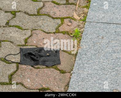 Entsorgte schmutzige schwarze medizinische Gesichtsmaske auf gemauertem Gehweg Stockfoto