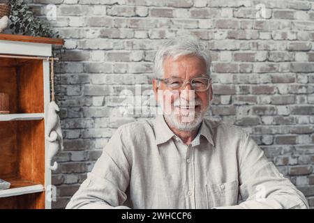 Kopffoto Porträt gutaussehender optimistischer Senior Mann sitzen Indoor schauend posierend vor der Kamera, mit breitem zahnigem Lächeln werben professionelle Zahnklinik Dienstleistungen für ältere. Das Konzept der sorgenfreien Altersversorgung Stockfoto