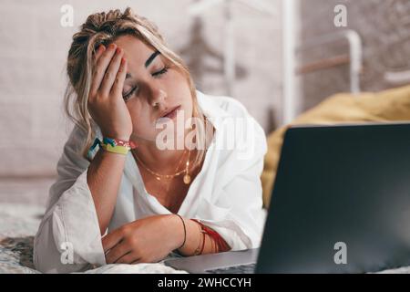 Nahaufnahme einer jungen Frau, die zu Hause im Schlafzimmer einen Laptop benutzte, schwere Kopfschmerzen hatte und sich nachts krank und erschöpft fühlte. Berühren Sie ihren Kopf massierend Stockfoto