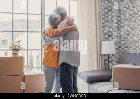 Glückliche dankbare ältere Frau, die Ehemann mit Liebe umschließt, Zuneigung in stapelbaren Kartons in der neuen Wohnung, feiert Immobilienkäufe, zieht in ein neues Zuhause Stockfoto