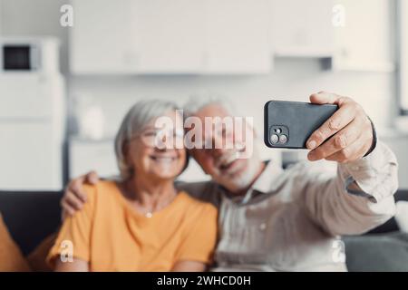 Glückliches altes Paar, das Selfie auf dem Handy macht, lächelnde ältere Ehepartner, Frau mittleren Alters und pensionierter Ehemann, der lacht, das Telefon hält, machen Selbstporträt auf der Smartphone-Kamera, konzentrieren Sie sich auf das mobile Display Stockfoto