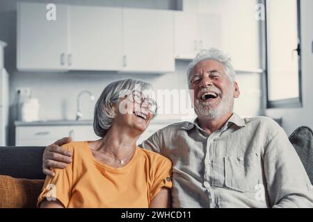 Glücklicher, reifer Mann und Frau sitzen zu Hause auf der Couch, umarmen und kuscheln, zeigen Fürsorge, lächelndes, liebevolles Seniorenpaar Entspannen Sie sich auf dem Sofa, genießen Sie ein zartes romantisches Familienwochenende zusammen Stockfoto