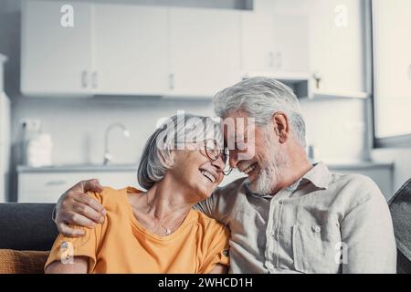 Glücklicher, reifer Mann und Frau sitzen zu Hause auf der Couch, umarmen und kuscheln, zeigen Fürsorge, lächelndes, liebevolles Seniorenpaar Entspannen Sie sich auf dem Sofa, genießen Sie ein zartes romantisches Familienwochenende zusammen Stockfoto