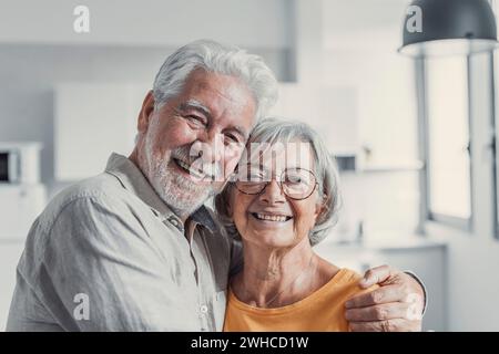 Kopfaufnahme Porträt lächelnder älterer 60er Jahre Ehemann und Ehefrau stehend Entspannen Umarmen Kuscheln, glückliches reifes altes Paar Ruhe im Wohnzimmer Umarmen Blick auf Kamera zeigen Liebe und Sorgfalt Stockfoto