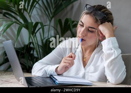 Porträt einer ernsthaften kaukasischen Studentin der Jahrtausendwende, die zu Hause am Schreibtisch sitzt und online auf einem Laptop studiert. Nachdenkliche junge attraktive Frau benutzen Computer Nehmen Sie Fernkurs oder Training. Bildungskonzept. Stockfoto