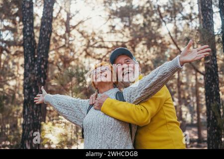 Porträt, Nahaufnahme eines alten, reiferen Paares, das die Bäume betrachtet und die Natur allein im Wald genießt. Rentner mit offenen Armen, die sich frei fühlen, Freiheitskonzept. Stockfoto