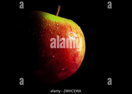 Roter Apfel mit grünen Flecken und Wassertröpfchen, dunkler Hintergrund Stockfoto