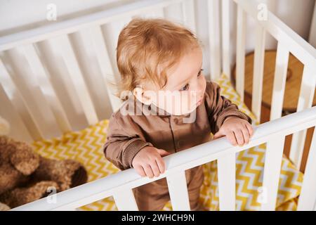 Blick aus der Höhe auf den niedlichen kleinen Jungen im Strampler, der im Kinderzimmer zu Hause steht, Kleinkind Stockfoto