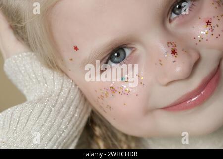 Porträt eines süßen kleinen blonden Mädchens mit blauen Augen und Glitzern im Gesicht. Stockfoto