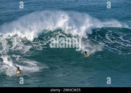 Ein Wasserski mit Stangen und neben ihm ein Jet Ski auf einer großen Welle, Nazare, Portugal Stockfoto