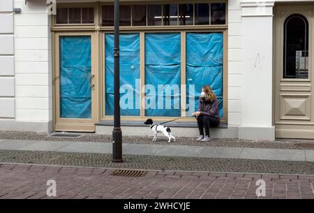 Eine Frau sitzt mit ihrem Hund vor einem geschlossenen Laden. Kunden, die in Einzelhandelsgeschäften in der Stadt einkaufen möchten, müssen einen negativen Corona-Test vorlegen Stockfoto