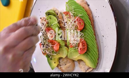 Avocado Toast mit kleinen Tomaten auf Roggenbrot Toast mit Weichkäse und Sprossen. Gesundes Frühstück Stockfoto