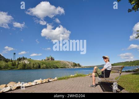 Frau sitzt auf einer Bank am Ufer des Upper Waterton Lake mit Blick auf das Prince of Wales Hotel, Waterton Lakes National Park, Alberta, Kanada Stockfoto