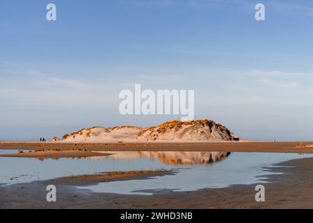 An einem ruhigen Tag spiegelt sich die Dünenlandschaft auf Norderney im Wasser wider, die Menschen im Hintergrund verwischen Stockfoto