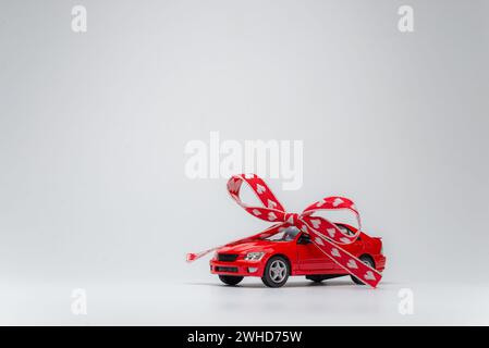 Rotes Modellauto mit Schleife auf weißem Hintergrund. Auto als Geschenk, Überraschung. Stockfoto