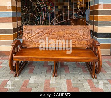 Costa Rica, San Jeronimo - 22. Juli, 20.23: El Jardin Souvenir Shop. Nahaufnahme, geformte braune Holzbank mit Pferden, Bäumen und einer Bergkette Stockfoto