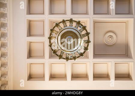 Großer Vintage-Kronleuchter mit Kerzenlampen, die an einer Holzdecke hängen. Metalldurchbrochener Rahmen mit geschmiedetem Ornament. Stockfoto