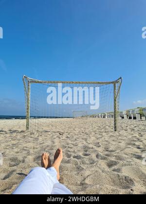 Frauenfüße entspannen in der Sonne am Meer, Blick durch das Fußballtor am Strand von Markgrafenheide, Ostsee, Deutschland Stockfoto