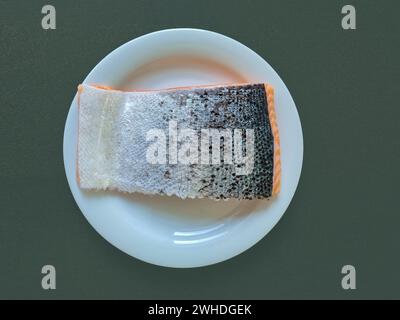 Ein Stück frischer Lachs liegt isoliert mit der silbernen Haut nach oben auf einer weißen Platte Stockfoto