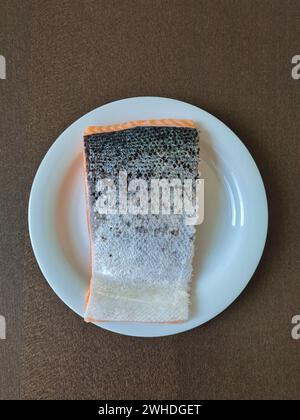 Ein Stück frischer Lachs liegt isoliert mit der silbernen Hautseite auf einer weißen Platte Stockfoto