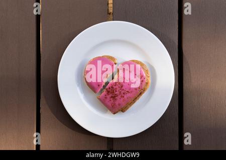 Symbolischer rosafarbener Herzkeks mit herzförmigem Riss auf einer weißen Platte zum Valentinstag Stockfoto