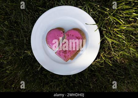 Symbolischer rosafarbener Herzkeks mit herzförmigem Riss auf einem weißen Teller zum Valentinstag Stockfoto