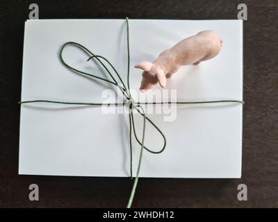 Ein Geschenk ist mit weißem Geschenkpapier, grünem Band und Klebeband mit einem kleinen rosafarbenen Spielzeugschwein dekoriert Stockfoto