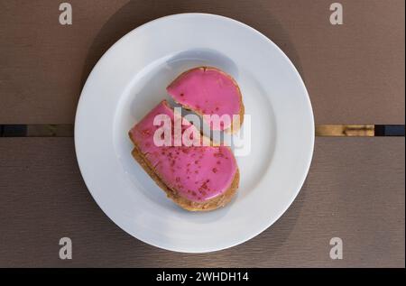 Symbolischer rosafarbener Herzkeks mit herzförmigem Riss auf einem weißen Teller zum Valentinstag Stockfoto