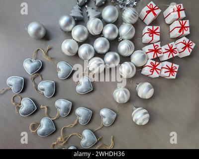 Silberne dekorative Herzen, silberne Weihnachtskugeln und weiße dekorative Anhänger liegen auf grauem Hintergrund vor der Weihnachtsdekoration Stockfoto