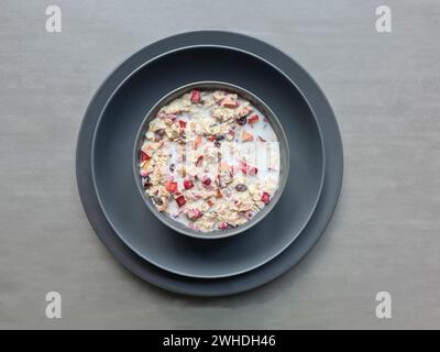 Müsli mit Milch in einer Schüssel auf zwei grauen Tellern zum Frühstück, Fruchtmüsli mit Körnern und getrocknetem Obst Stockfoto