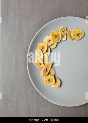 Bananenchips auf einem hellgrauen Teller als Nachtisch und Snack zwischen den Mahlzeiten Stockfoto