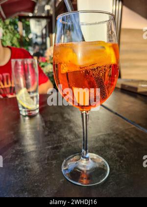 Das alkoholische Erfrischungsgetränk Aperol Spritz wird auf einen Tisch neben einem Glas Mineralwasser gestellt Stockfoto