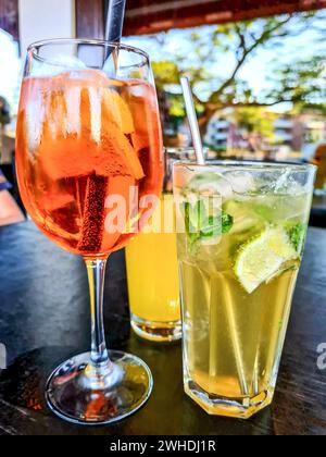 Das alkoholische Erfrischungsgetränk Aperol Spritz wird auf einem Tisch neben einer alkoholfreien Mücke und einer Limonade platziert Stockfoto