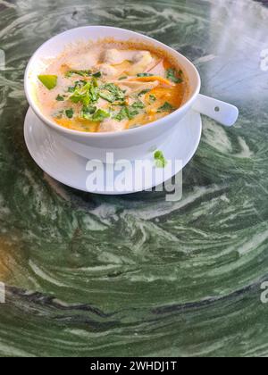 Tom Kha Gai, Hühnersuppe in einer weißen Schüssel, enthält die Zutaten Kokosmilch, Galgant, Zitronengras, Hühnchen, Lauch und Petersilie Stockfoto