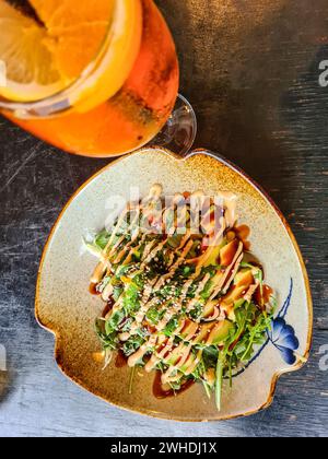 Ein orangenfarbenes alkoholisches Sommergetränk und Avocadosalat mit Sesamsamen im Restaurant Stockfoto