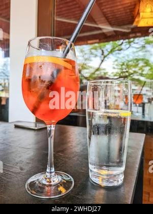 Das alkoholische Erfrischungsgetränk Aperol Spritz wird auf einen Tisch neben einem Glas Mineralwasser gestellt Stockfoto