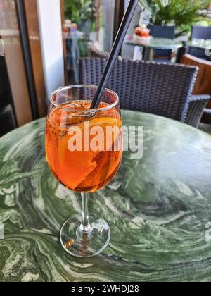 Das alkoholische Erfrischungsgetränk Aperol Spritz mit einer Orangenscheibe im Glas und einem schwarzen Strohhalm steht allein auf einem Tisch vor dem Restaurant Stockfoto