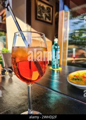 Das alkoholische Erfrischungsgetränk Aperol Spritz wird auf einen Tisch neben einem Glas Mineralwasser gestellt Stockfoto