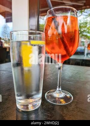 Das alkoholische Erfrischungsgetränk Aperol Spritz wird auf einen Tisch neben einem Glas Mineralwasser gestellt Stockfoto