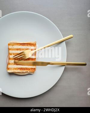 Ein Sandwich mit gegrilltem Schinken und Streifenmuster liegt auf einem hellgrauen Teller vor grauem Hintergrund Stockfoto