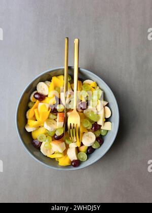 In Scheiben geschnittene Äpfel und Mangohorangentrauben als Obstsalat in einer Schüssel mit Messer und Gabel serviert Stockfoto