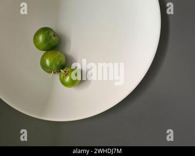 3 kleine grüne Tomaten auf einem weißen Teller auf grauem Hintergrund Stockfoto