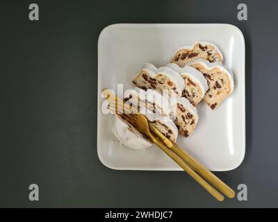 In der Adventszeit vor Weihnachten liegen mehrere Stück Weihnachtskuchen auf einem quadratischen weißen Porzellanteller mit goldenem Besteck Stockfoto