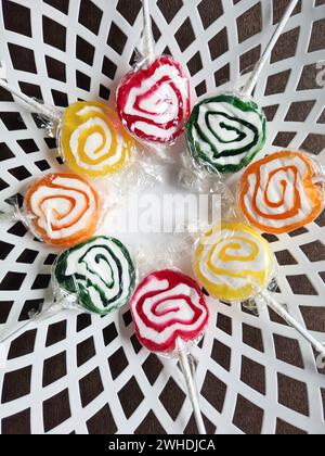 Acht Lollies sind noch immer in Plastikfolie im Kreis auf einer weißen Schüssel gewickelt Stockfoto
