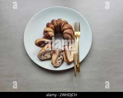 Stücke geschnittener Marmorkuchen liegen auf dem hellgrauen Teller neben dem goldenen Besteck Stockfoto