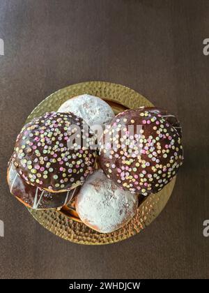 Pfannkuchen mit Schokoladenglasur und Streuseln und mit Puderzucker, bekannt als Donuts für Karneval Stockfoto