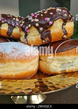 Nahaufnahme von Pfannkuchen mit Schokoladenglasur und Streuseln sowie Puderzucker, bekannt als Donuts für Karneval Stockfoto